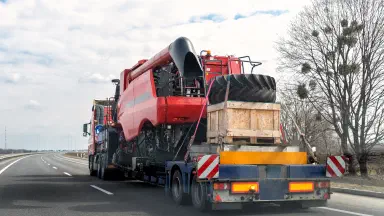 Heavy industrial truck with semi trailer platform transport disassembled combine harvester machine on common public highway road on sunset sunrise day. Agricultural equipment transportation service