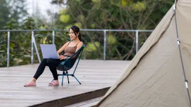 Woman working on laptop outside a tent.